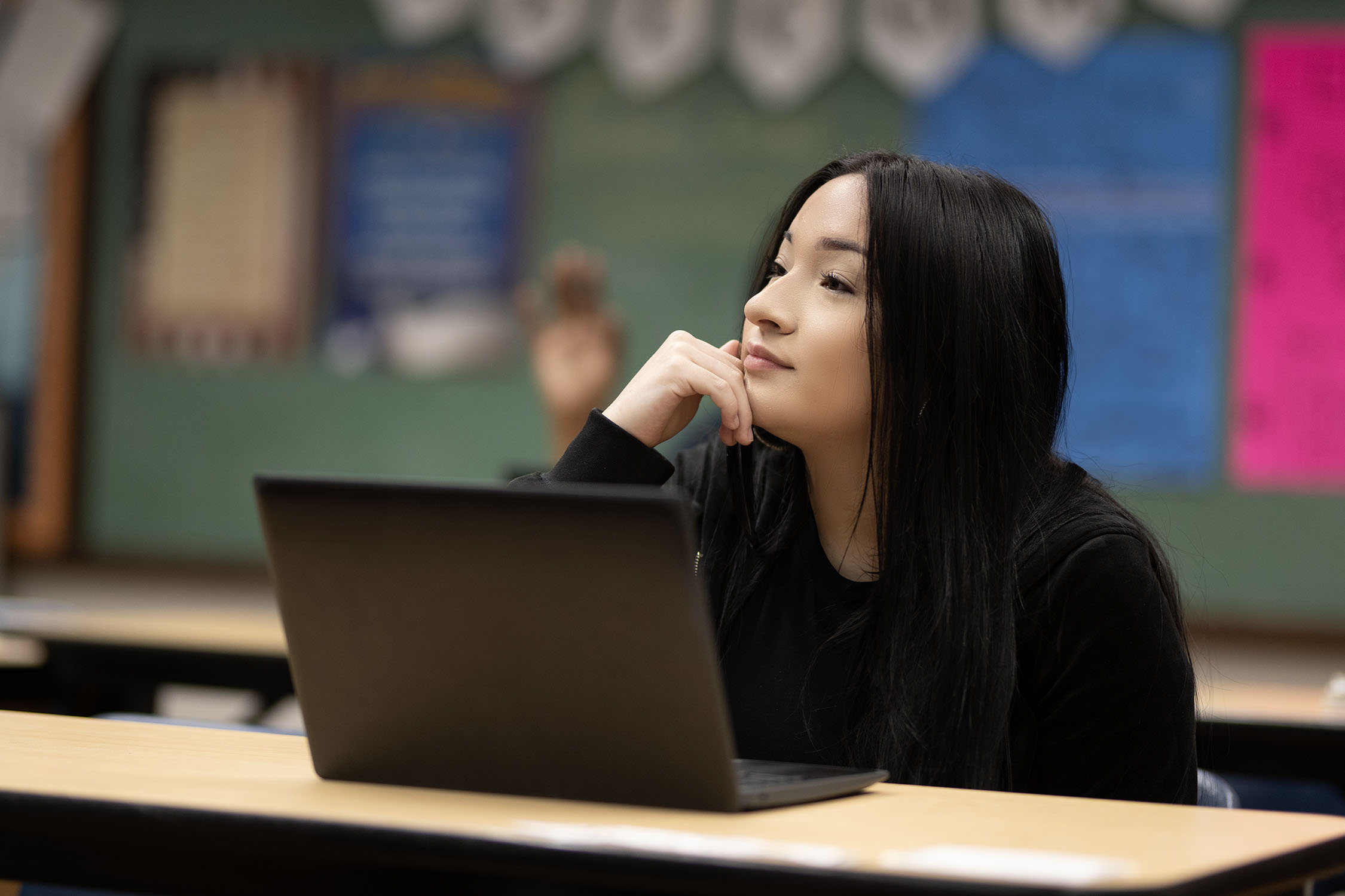 Woman pondering while working on laptop in classroom