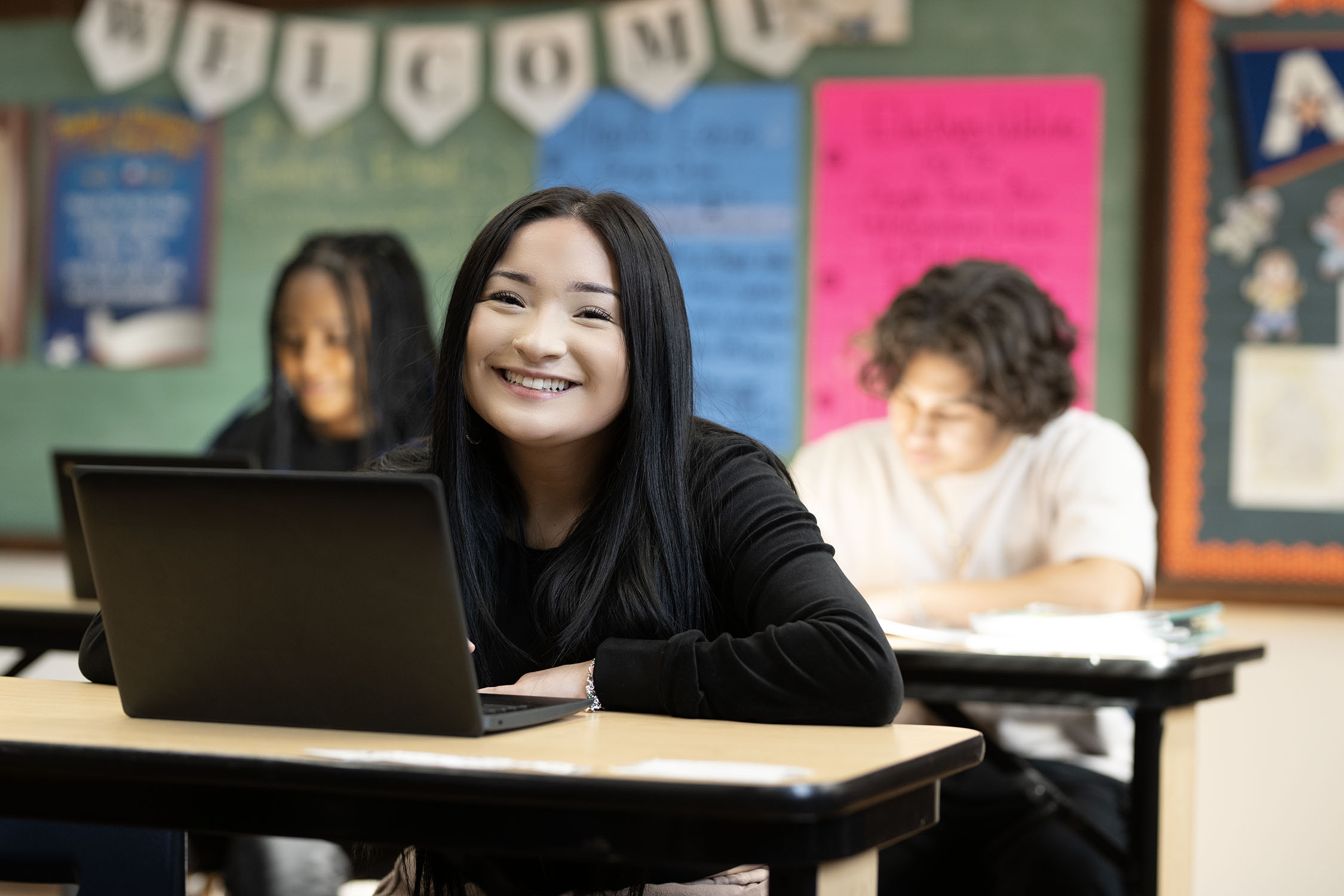 Smiling student using laptop in classroom setting