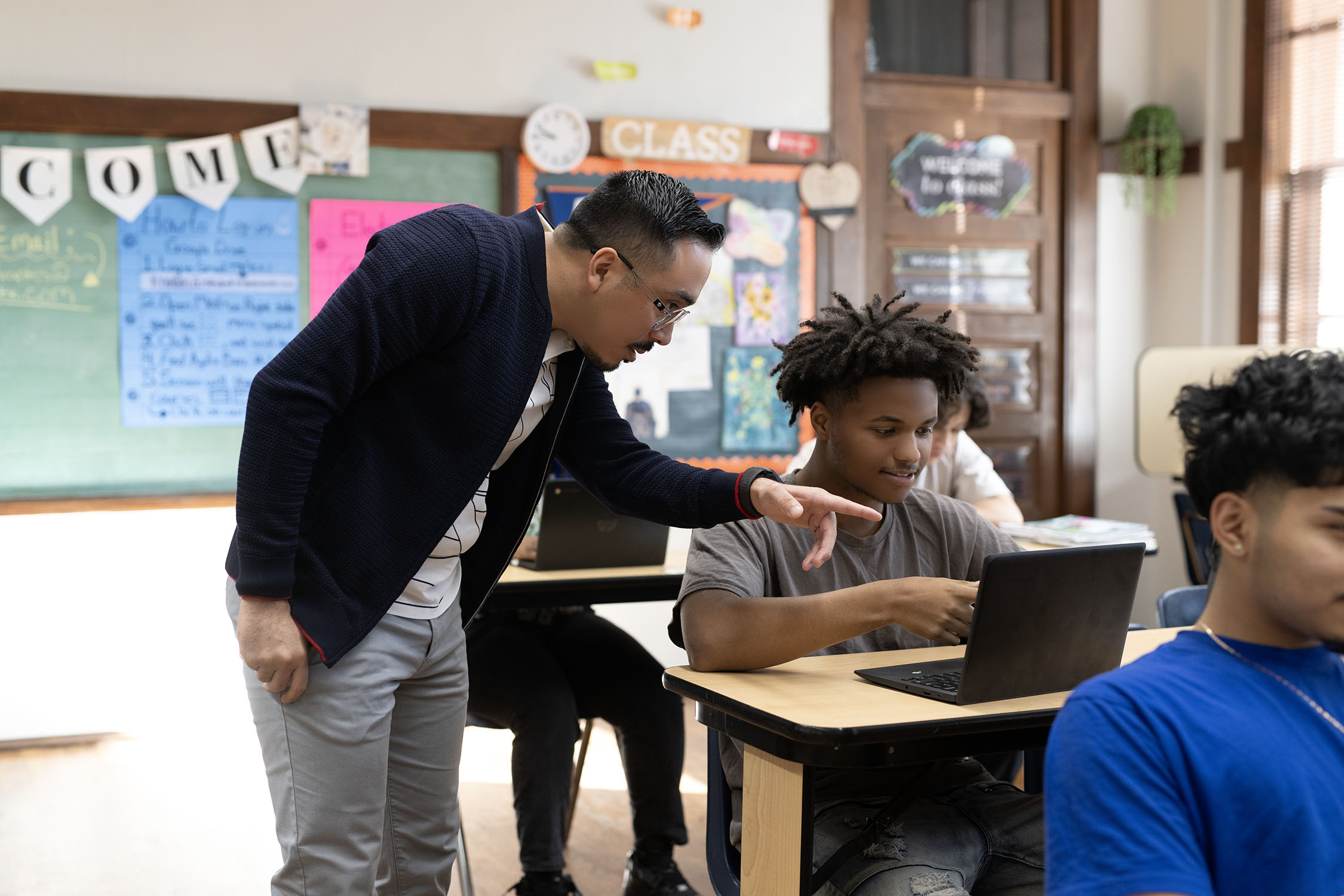 Teacher assisting student with laptop in classroom