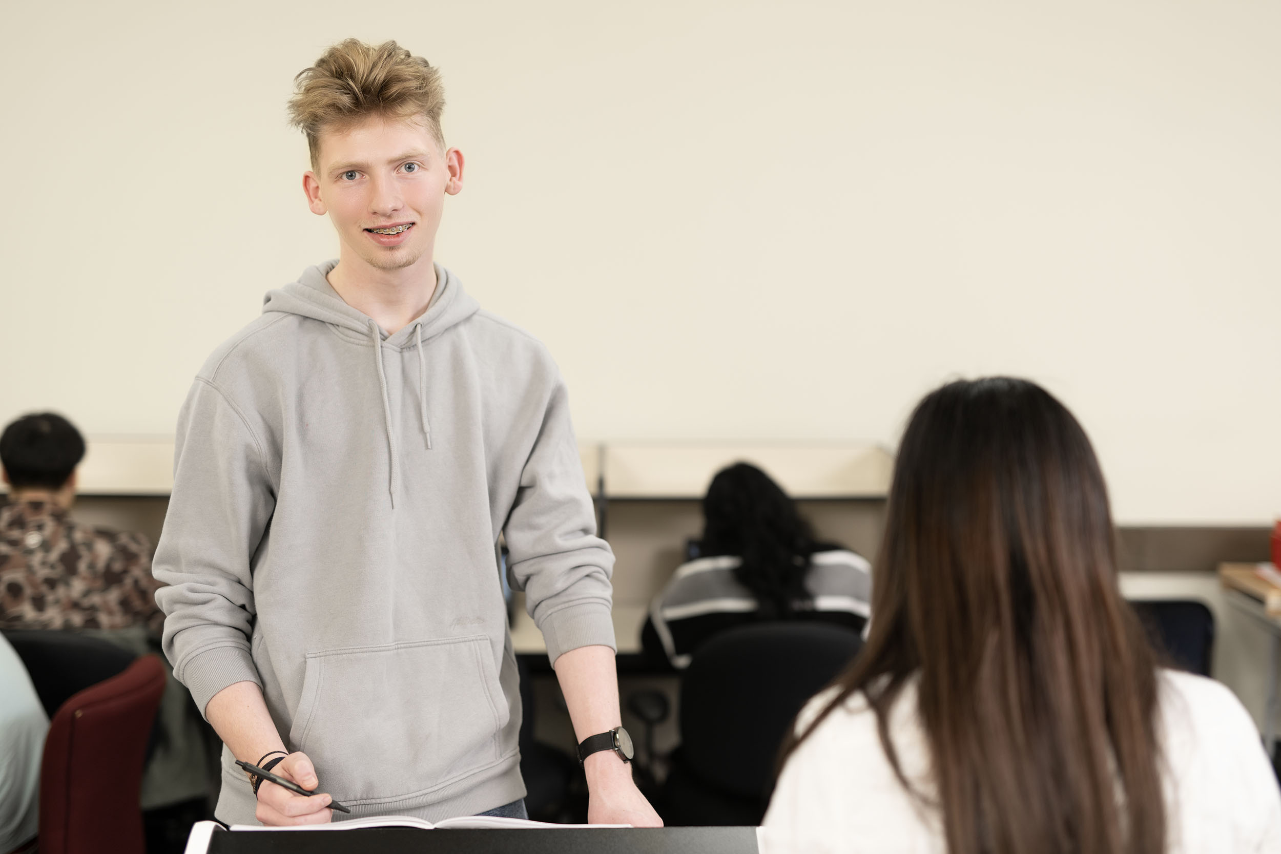 Young male student standing in a classroom setting.
