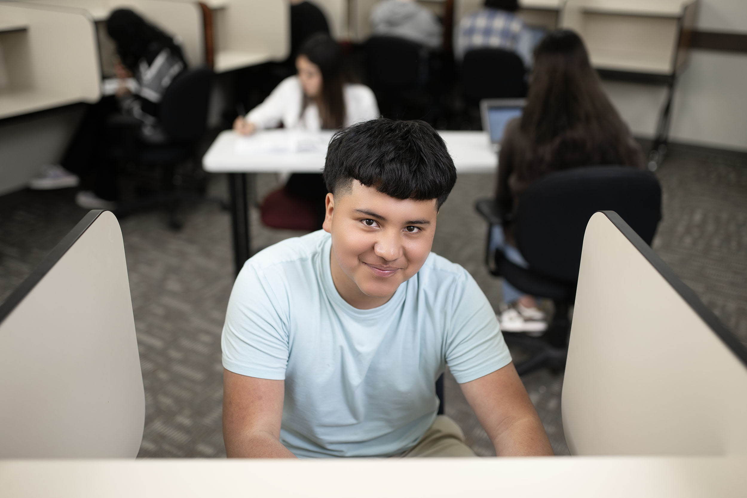 Student smiling in classroom with peers studying behind