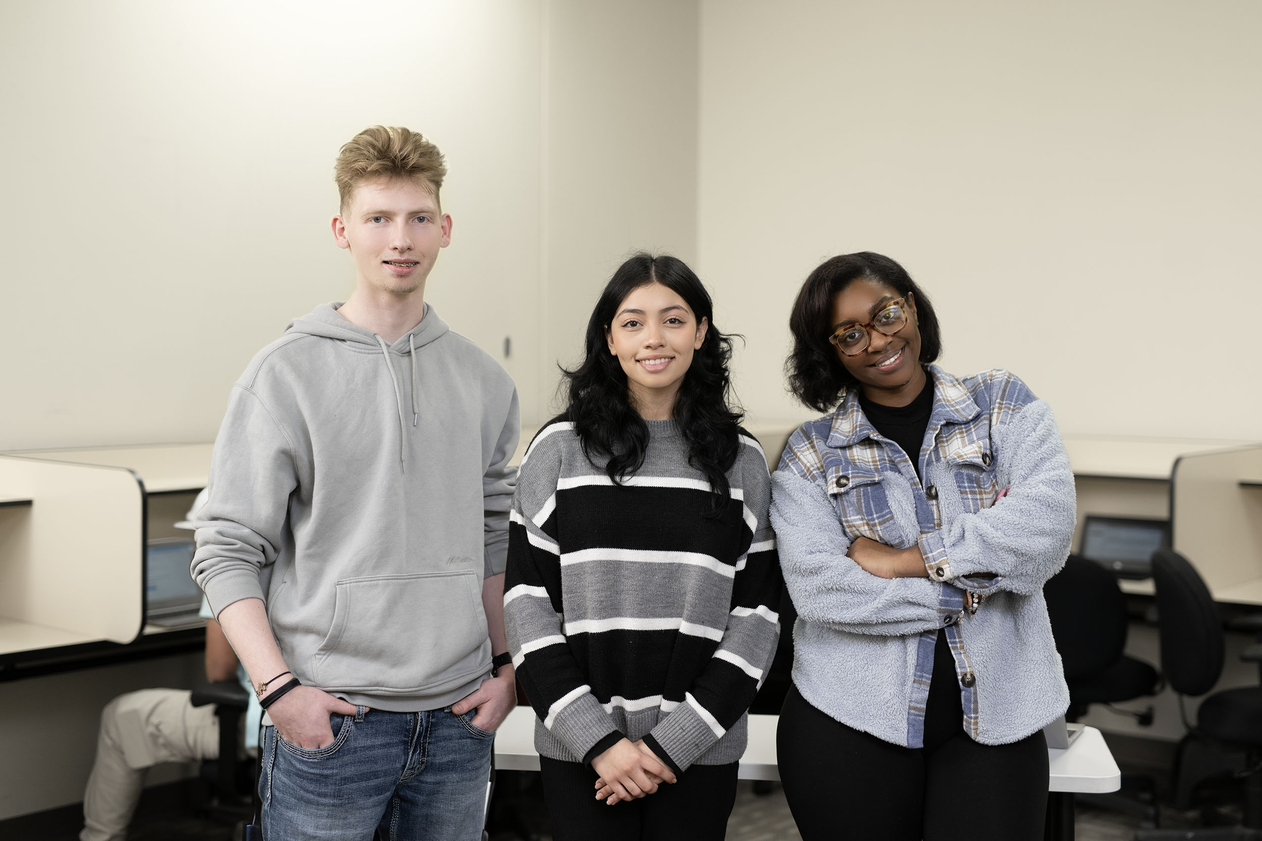 Three students smiling in a classroom setting.