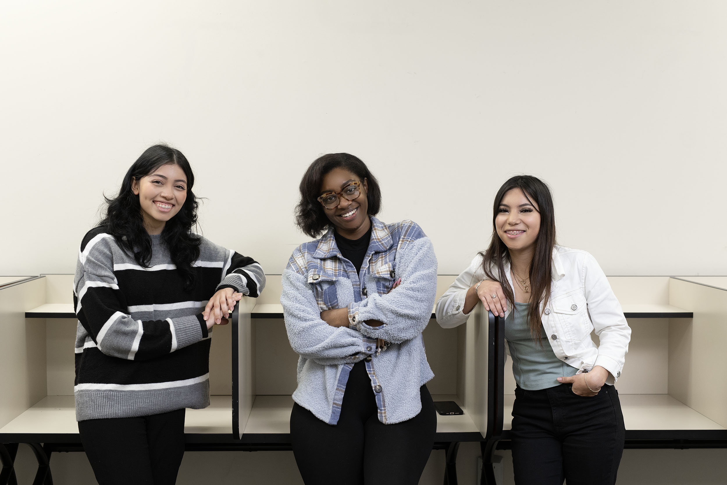 Three smiling women leaning on a desk indoors