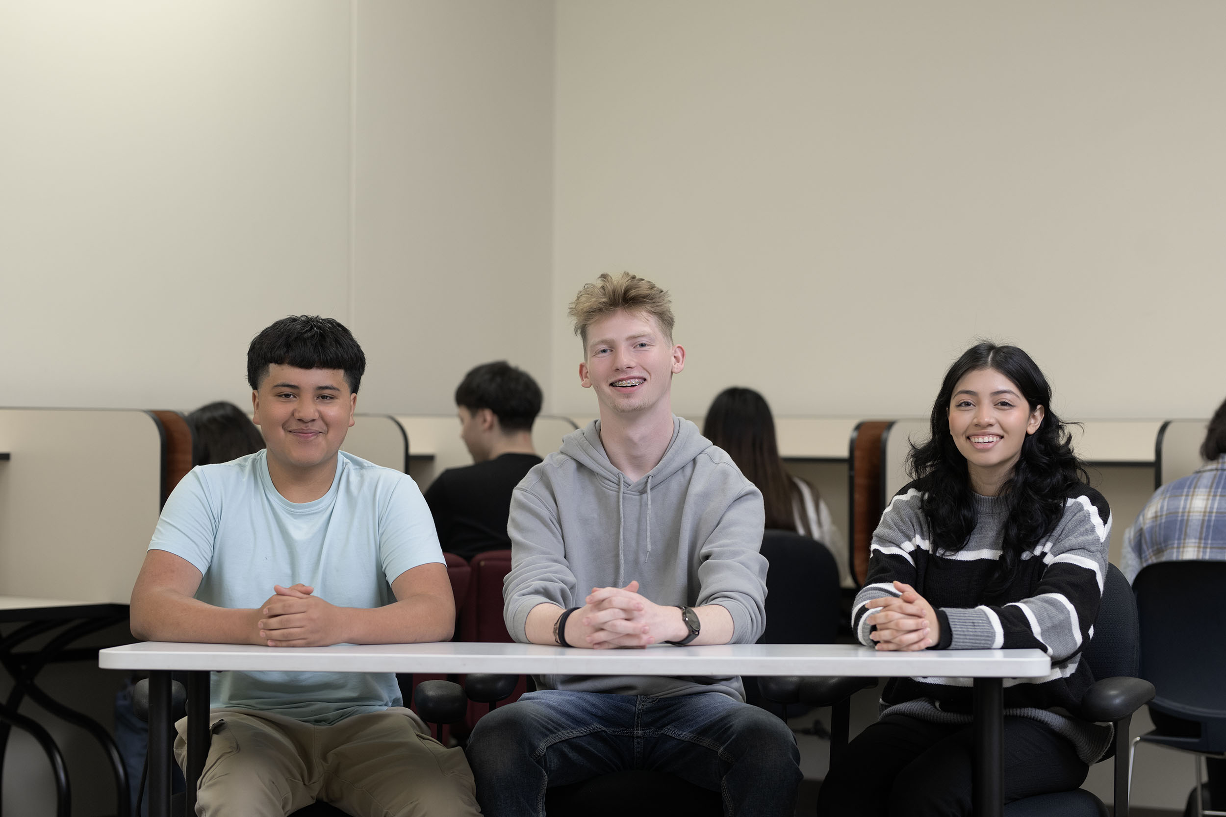 Three students smiling sitting in classroom