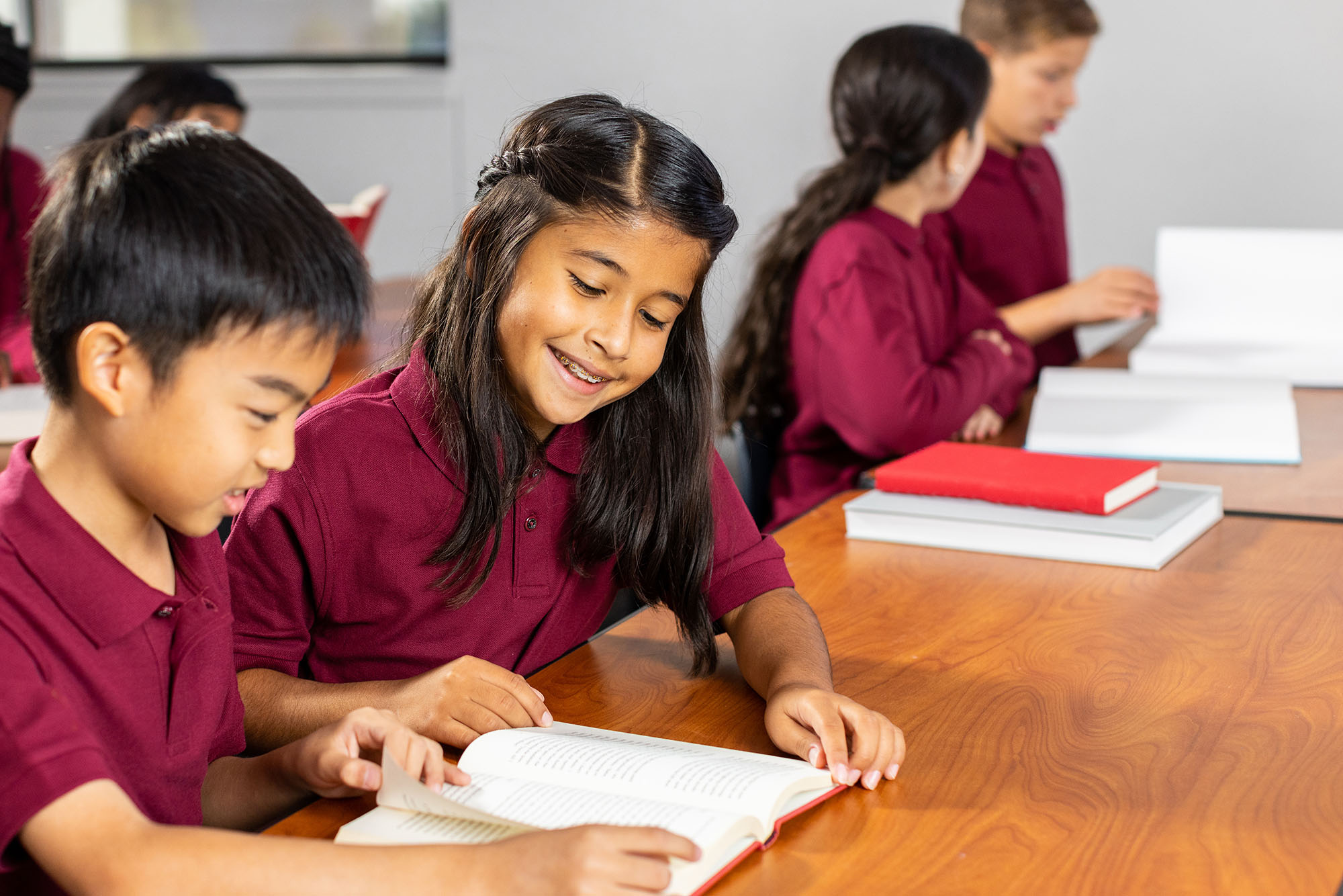 Students in uniforms reading book in classroom