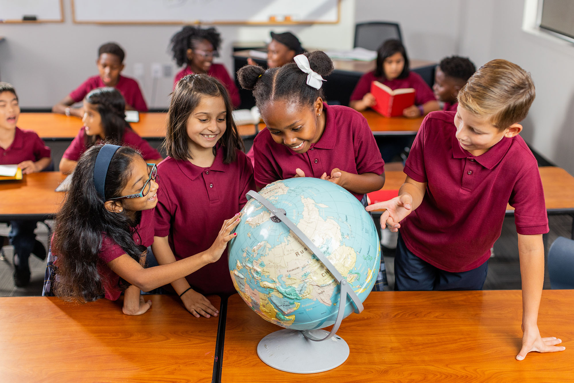 Students in uniforms examining a globe in classroom