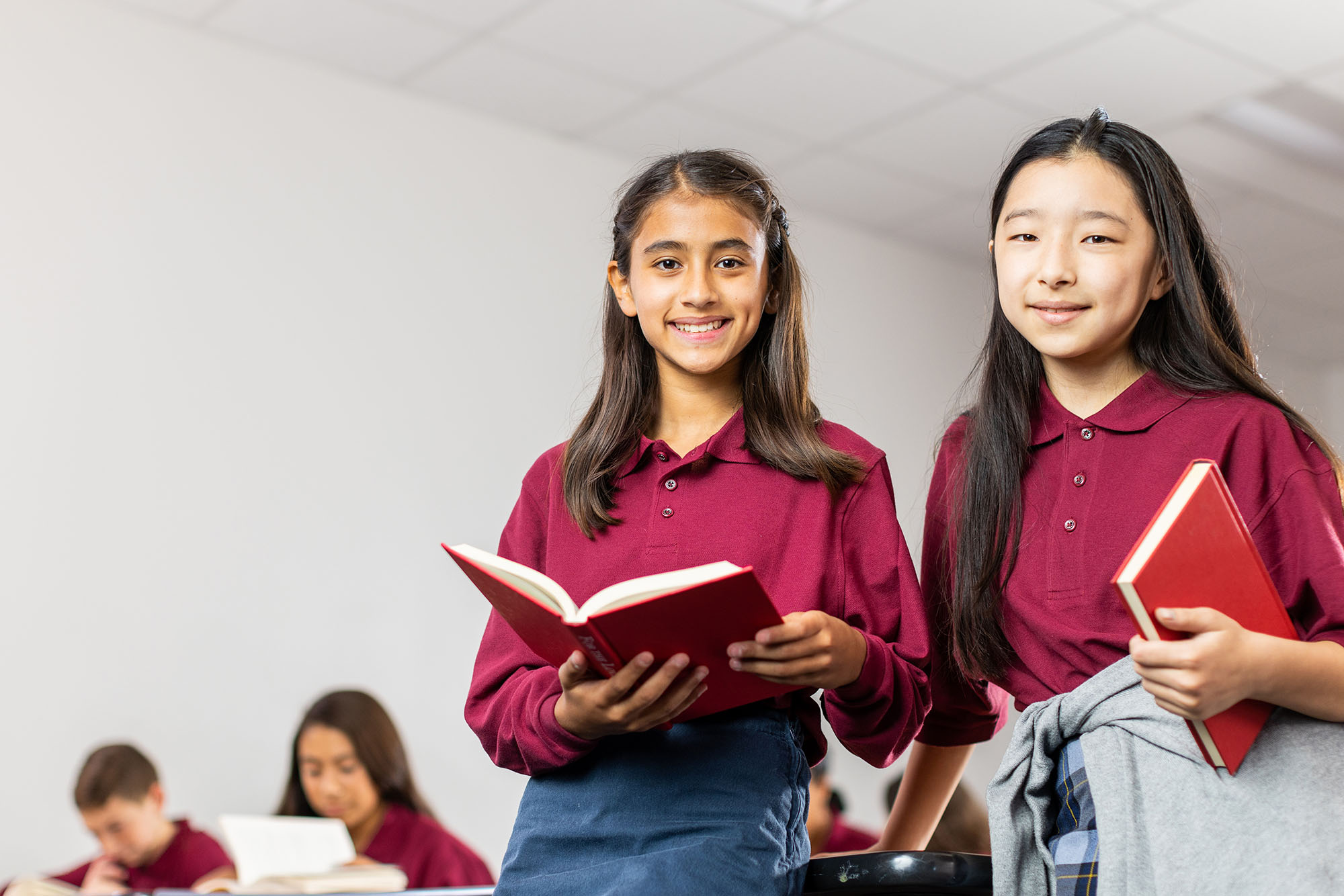 Two students in uniform reading books in class