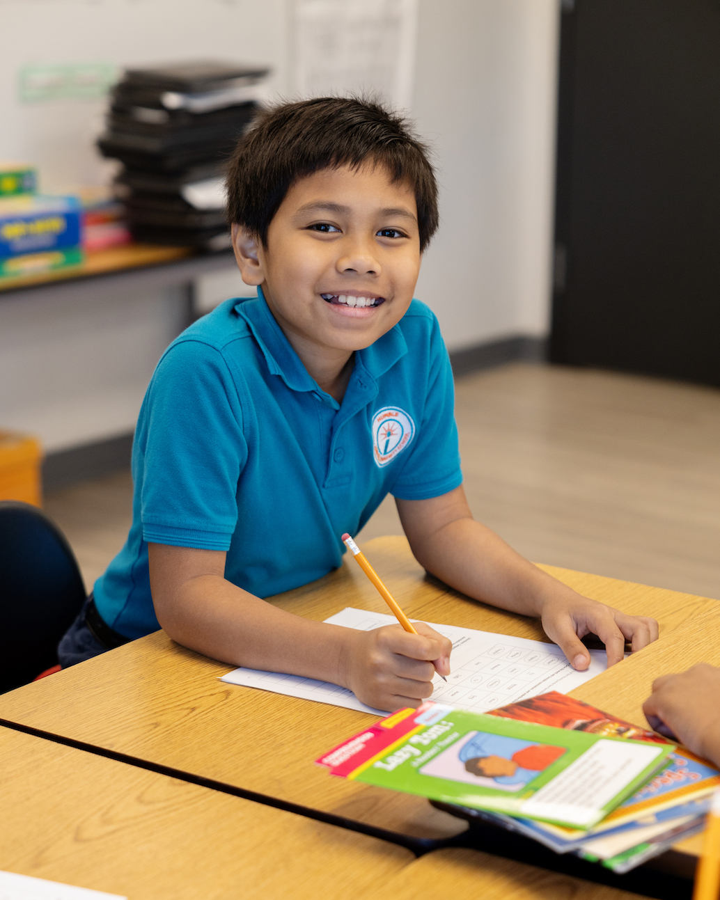 Smiling child writing at classroom desk happily.